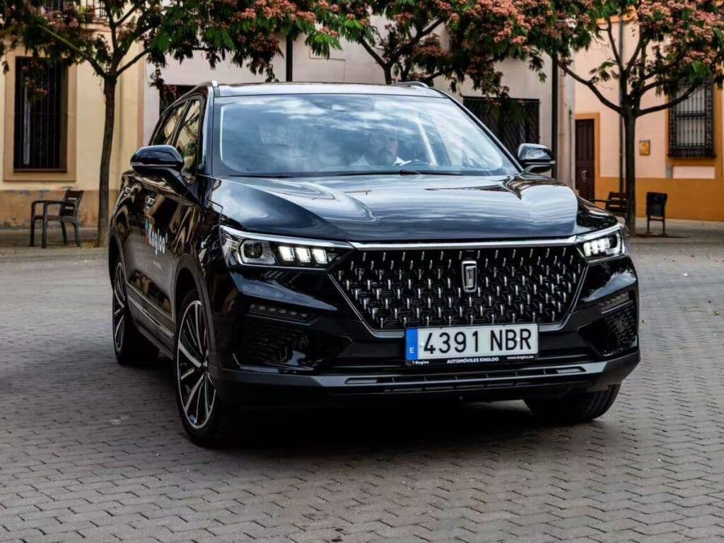 SUV negro brillante estacionado en una calle empedrada con árboles en flor al fondo.